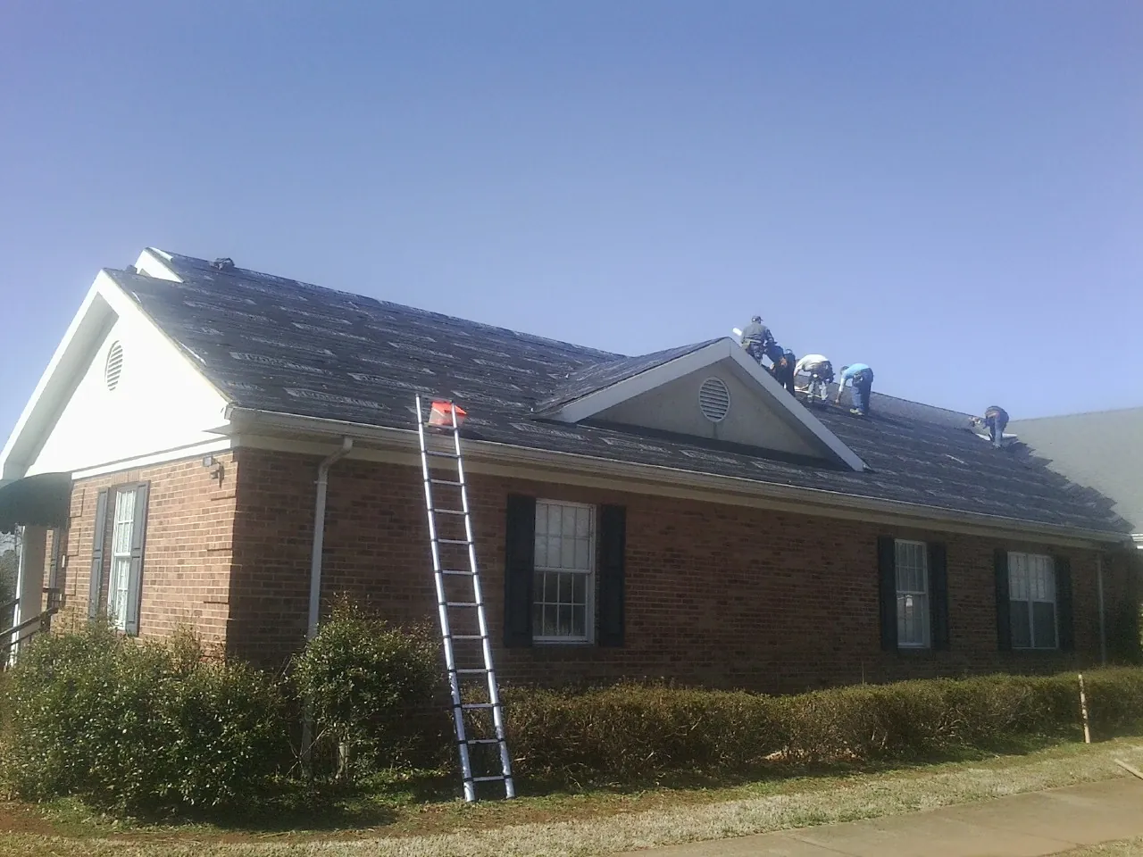 Crew tearing shingles off a brick ranch roof with a ladder set — Metal Roof Repair work by our crew in Yorkshire