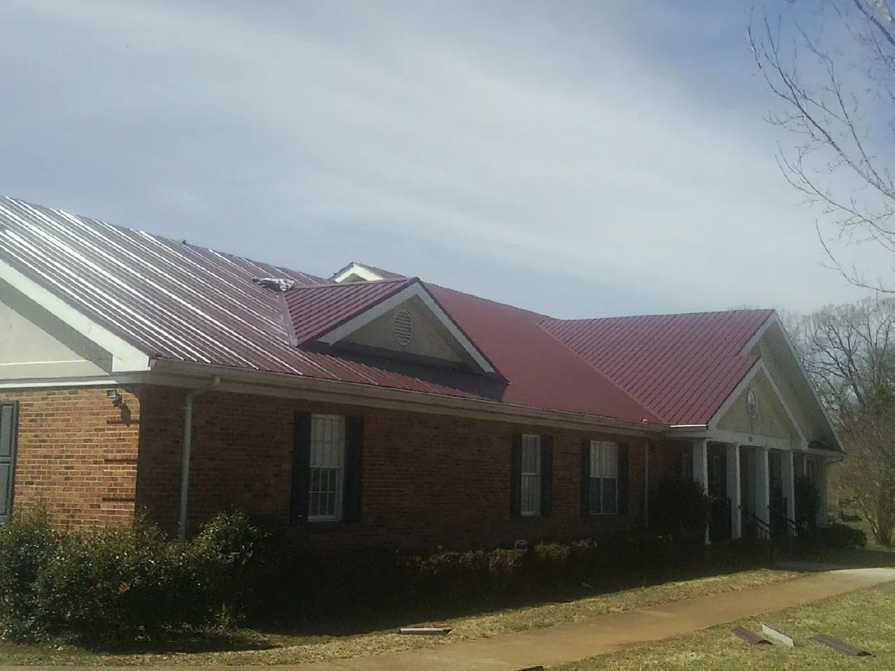 Red metal roof with gabled entries on a long brick building, from a Hail Damage Roof Repair job in Yorkshire
