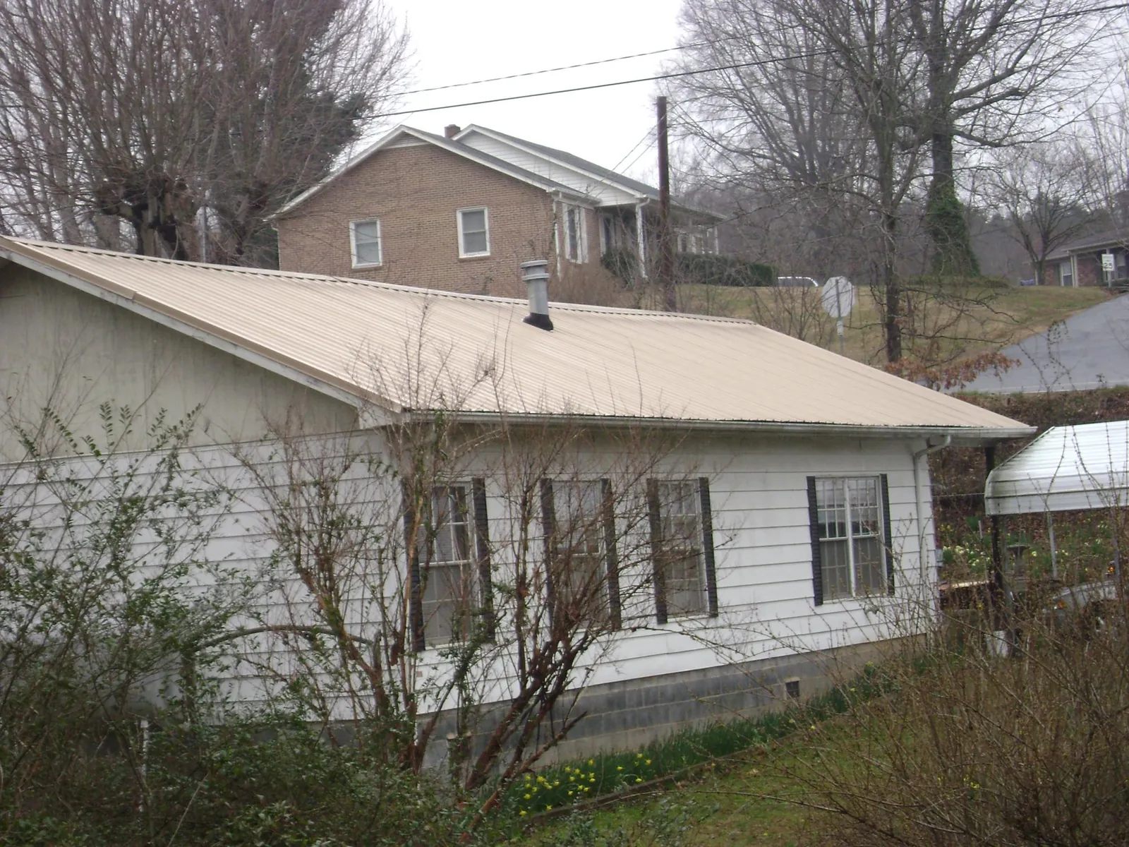 Tan metal roof on a white sided house set into a hillside — Commercial Roofing by Roofing Brothers in Yorkshire